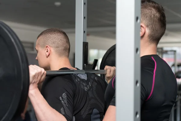 Gym Coach Helping Man On Barbell Squat