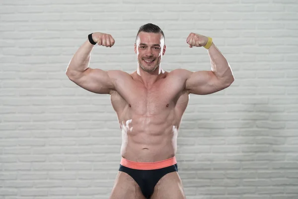Muscular Man Flexing Muscles On White Bricks Background
