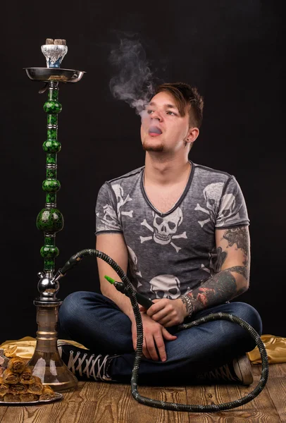 Tattooed man smoking traditional hookah.