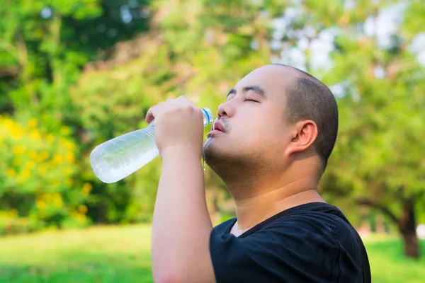 An Asian Thai bald head guy is pouring water drink into his mouth to prevent thirst and heatstroke