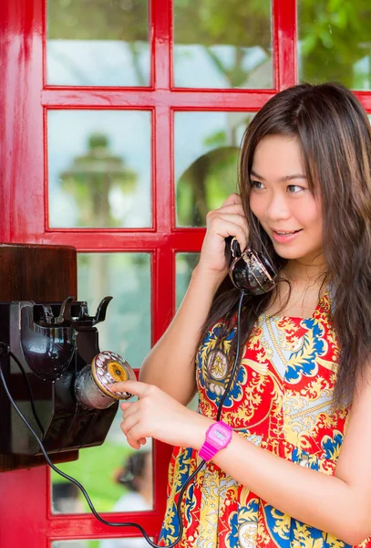 Asian Thai girl is talking with an old-fashion phone in the telephone booth in vintage retro fashion style.