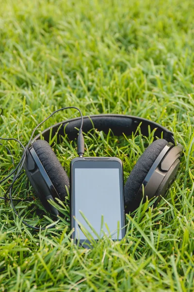 Black Smartphone and Headphones on the Green Grass
