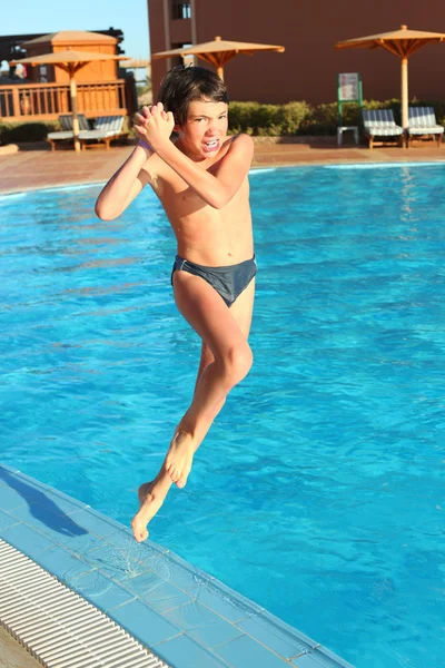 Preteen little boy jump into open air swimming pool