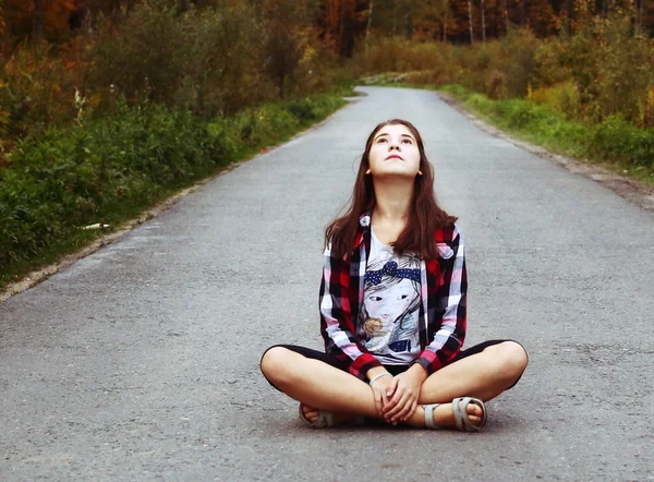 Beautiful teen girl sit on the country empty road