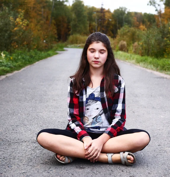Beautiful teen girl sit on the country empty road