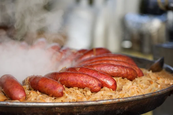 Fresh sausages with cabbage cooking in street market kitchen with blurry background, traditional russian meal with sausage, cabbage, carrots, traditional east region food