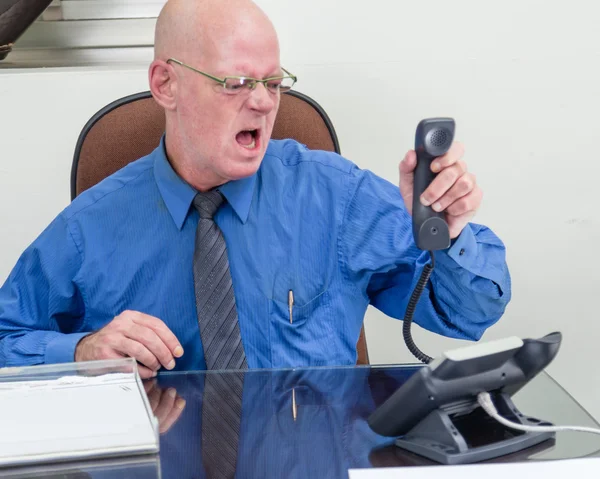 Businessman on phone at desk, angry