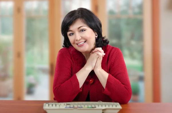 Cheerful mature woman in red knitted jacket sits at the desk