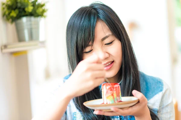 Smiling asian woman eating some strawberry cake in bakery cafe