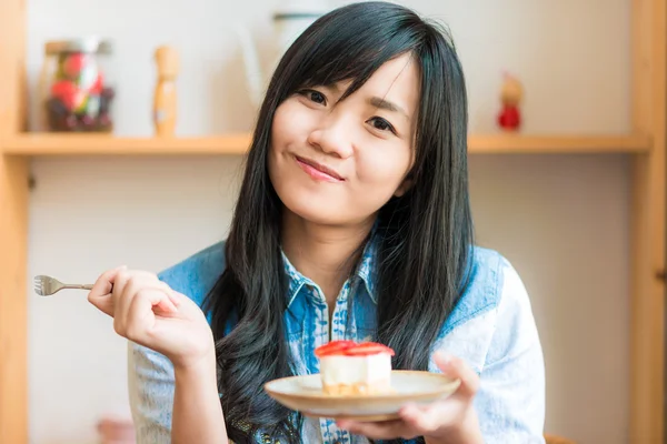 Smiling asian woman eating some strawberry cake in bakery cafe