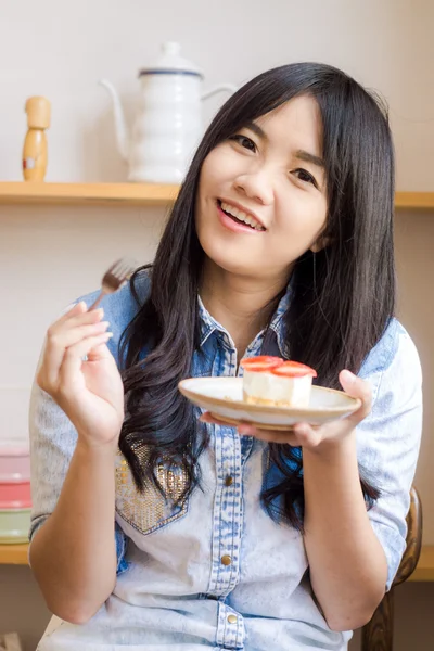 Asian smiling woman wearing jean shirt biting the piece of tasty