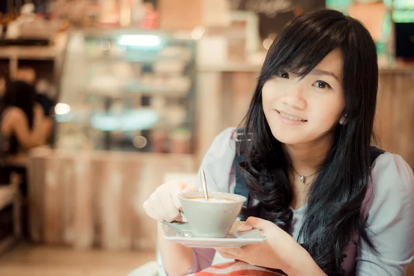 Beautiful asian young woman with coffee cup looking to camera at