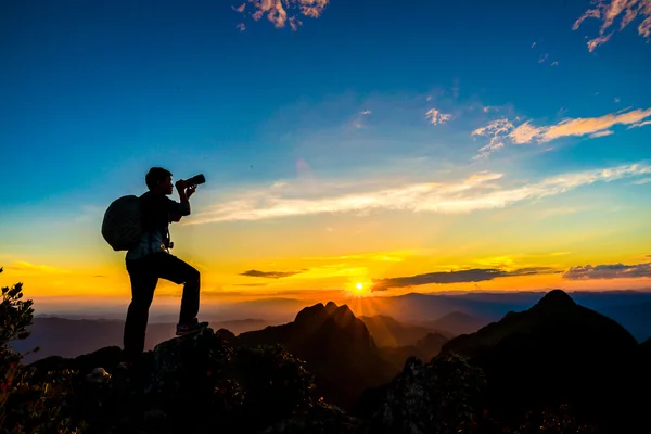 Photographer man on mountain reaches for the sun