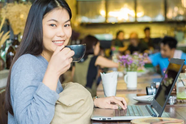Smiling asian women work on laptop at cafe