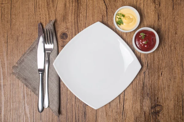 Empty plate with fork and knife, ketchup and mayonnaise