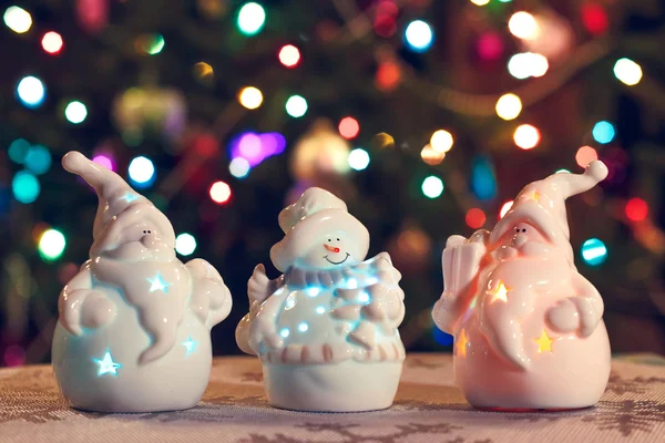 Illuminated Snowman and Jack Frost (Santa Claus) dolls in front of Christmas tree lights that are defocused, blurred background