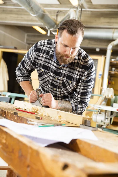 Carpenter work with plane on wood plank in workshop