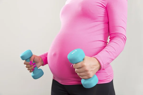 Pregnant woman exercising with training weights indoor