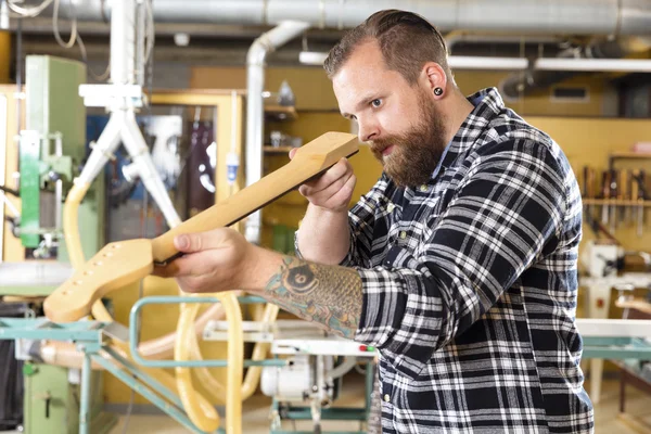 Carpenter inspects a wooden guitar neck in workshop