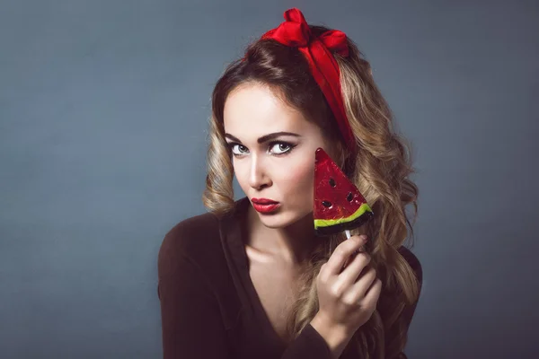 Portrait of beautiful young sexy blonde with a red armband with red lips with lollipop  form watermelon lollipop licking tongue sensual temptation to make up pin up