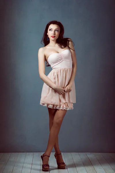 Sexy young beautiful brunette with long hair, with a slender figure standing on a lifting leg up holding his heel in a pink dress and retro women athletic and acrobatic pin up make-up