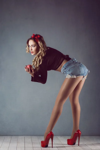 Beautiful young sexy blonde slim figure with a red armband with red lips in denim shorts in red high heels with long legs Pin Up