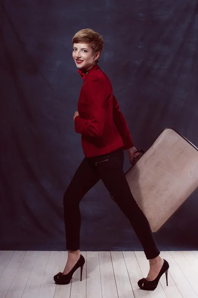 Young sexy girl with a suitcase in a jacket and pants in bow tie with makeup movement is in a hurry