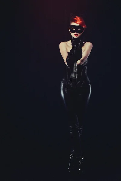 Cat woman with red hair in a leather suit with ears of a cat with a mask and makeup leather gloves
