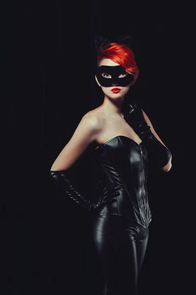 Cat woman with red hair in a leather suit with ears of a cat with a mask and makeup leather gloves