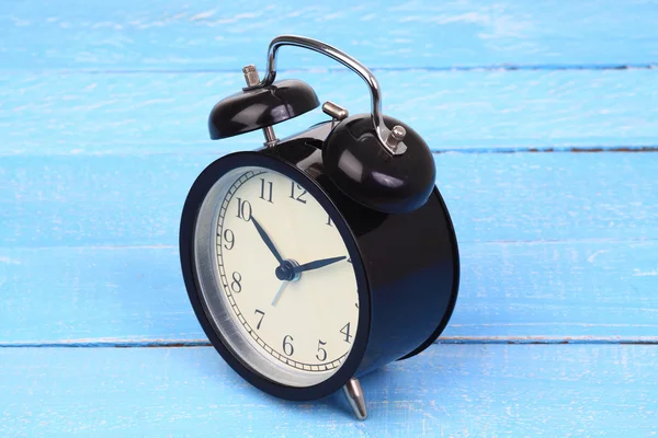 Classic alarm clock on blue wood background.