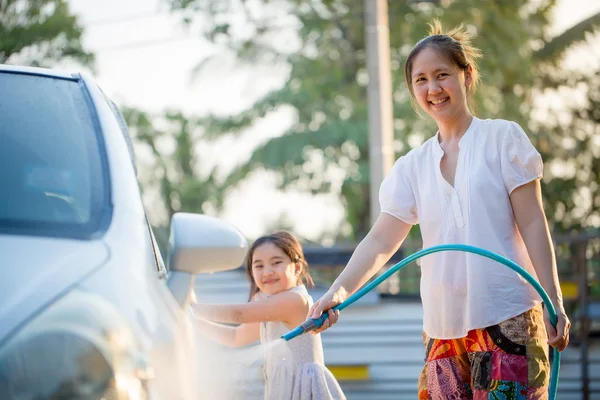 Happy Asian girl washing car with her mother at home