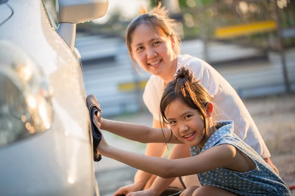 Happy Asian girl washing car with her mother at home
