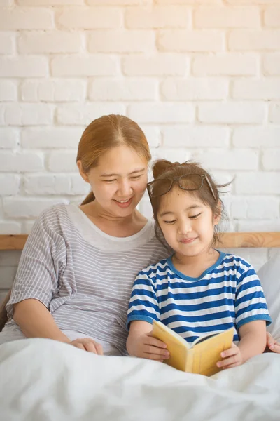 Happy Asian girl reading story book with her mother together