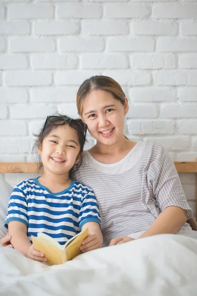 Happy Asian girl reading story book with her mother together