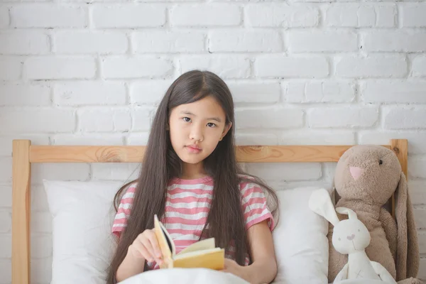 Asian girl reading story book on the bed