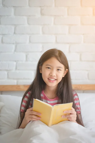 Asian girl reading story book on the bed
