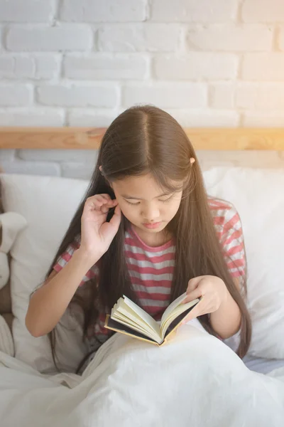 Asian girl reading story book on the bed