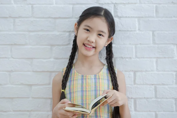 Asian girl reading story book on white brick wall