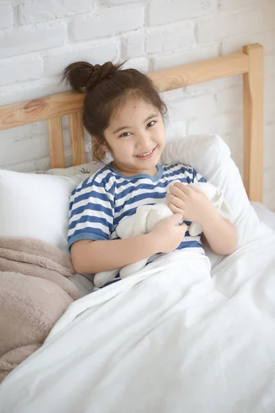 Little Asian girl hugging the doll on the bed