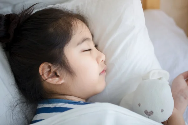 Little Asian girl hugging the doll and sleeping on the bed