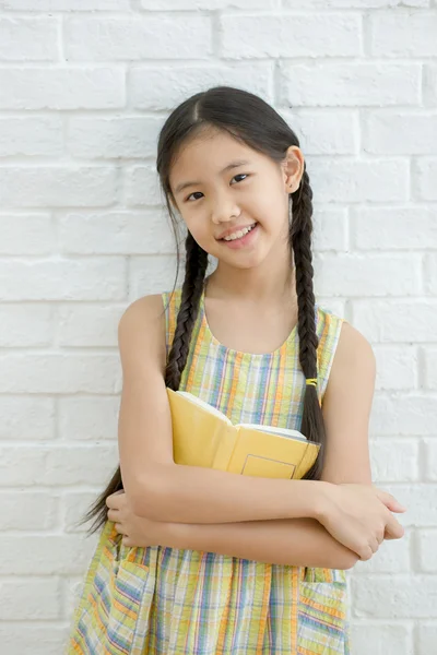 Happy Asian girl reading story book on white brick wall