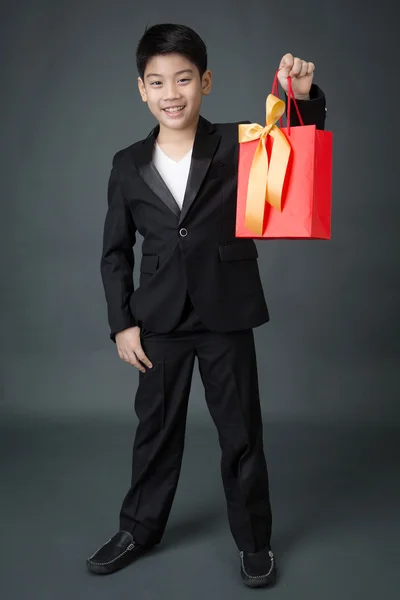 Portrait of asian boy in black suit holding gift bag