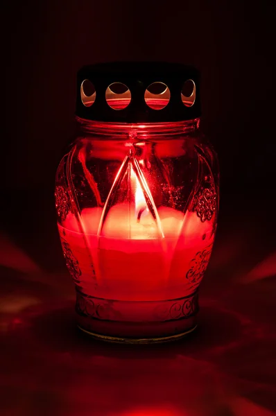 Red burning votive candle in the dark