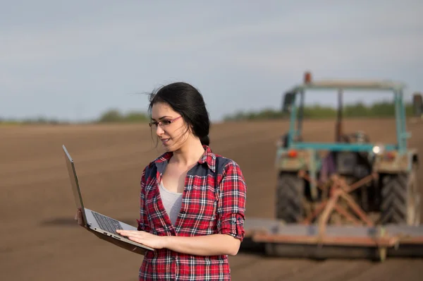 Farmer girl with laptop in field with tractor