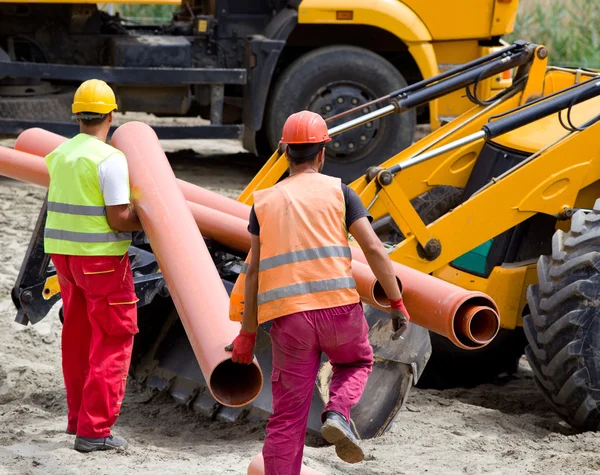 Workers loading bulldozer with pipes