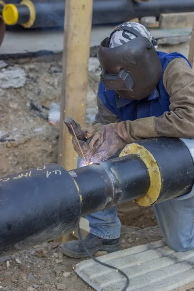Welder welding underground steel pipe kneels on ground 3