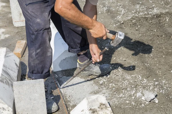 Worker using chisel and hammer for paving work