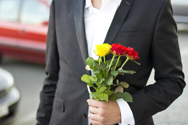 Brutal man in a black suit and white shirt with a bouquet of roses in hands