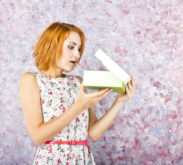 Young girl with red hair with a gift on a bright background. Portrait of a beautiful girl.