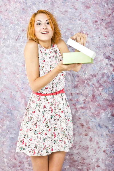 Young girl with red hair with a gift on a bright background. Portrait of a beautiful girl.